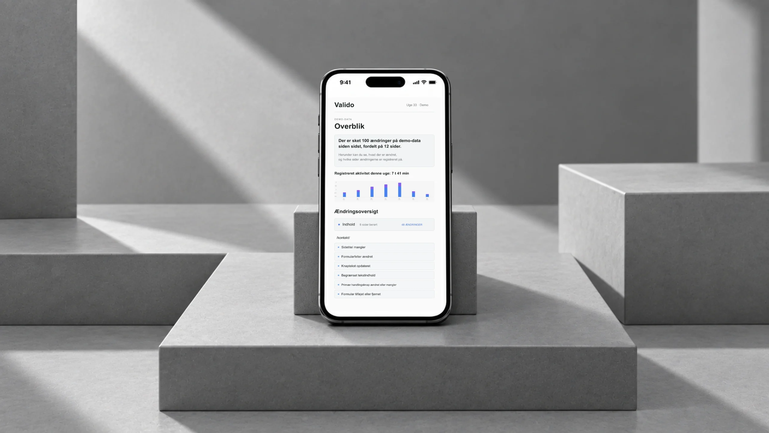 Valido: demo-SEO-rapport med aktivitetsgraf og ændringsoversigt på en sort telefon på grå, skulpturelle trin.