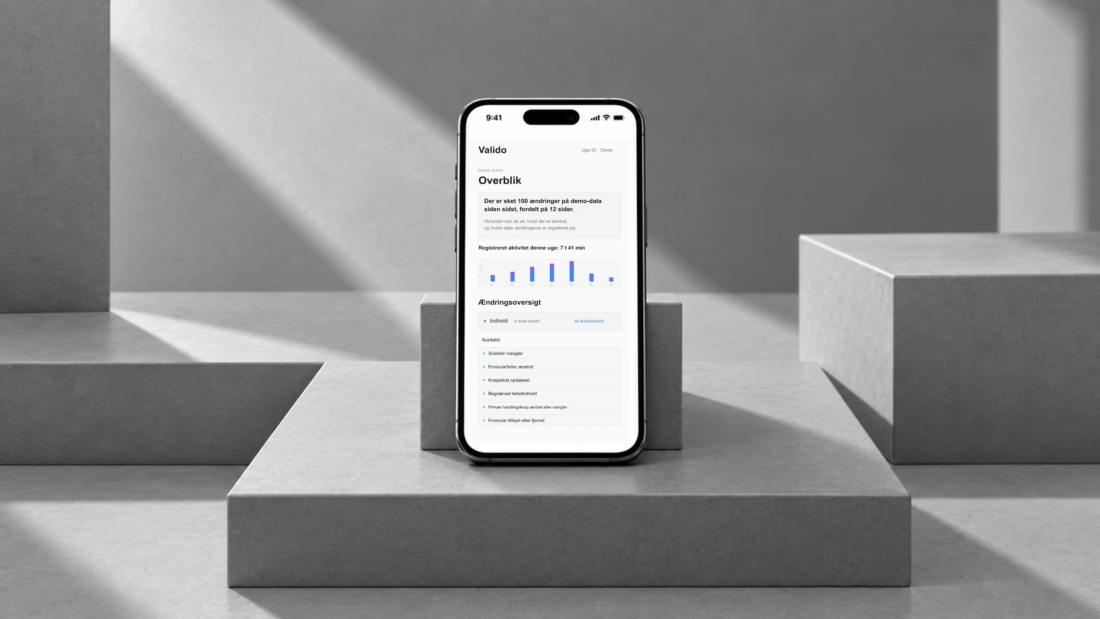 Valido: demo-SEO-rapport med aktivitetsgraf og ændringsoversigt på en sort telefon på grå, skulpturelle trin.